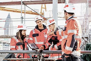 A group of people wearing helmets look at a tablet together