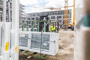 Mann in gelber Weste auf einem Gabelstapler mit Glasfenstern. Baustelle mit gelbem Kran im Hintergrund