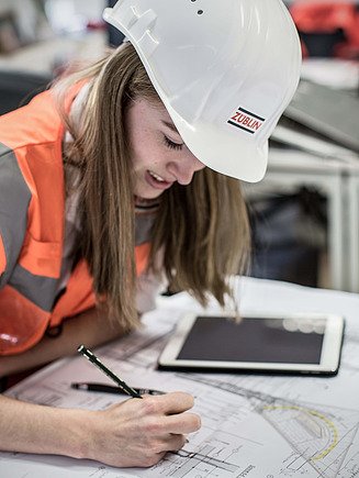 Woman with construction worker helmet and protective suit draws in a construction plan