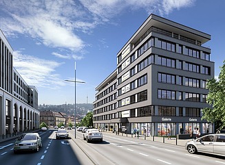 Vierspurige Straße mit grauem Gebäude, unten Ladengeschäfte, darüber 5 Etagen, die oberste springt etwas zurück und hat einen umlaufenden Balkon