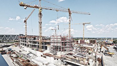 Cranes and skyscrapers under construction from a frog's-eye view against a blue sky