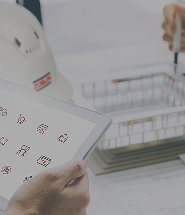 OpenTools Header Nahaufnahme eines Schreibtischs mit Züblin Helm, zwei Hände halten ein Pad mit den Icons für OpenTools, die Hände einer weiteren Person mit Stift