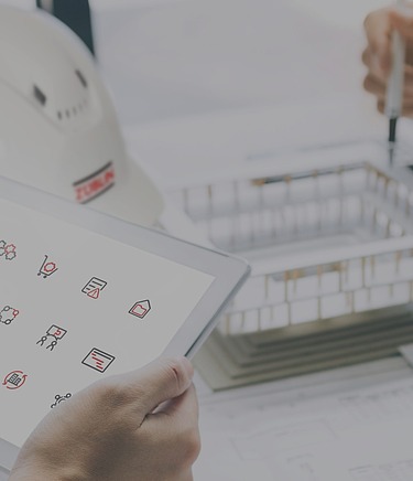 Close-up of a desk with Züblin helmet, two hands holding a pad with the icons for OpenTools, the hands of another person with a pen