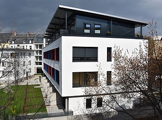 White residential building with many windows, partly accentuated in red and blue, attic with sloping roof on pillars