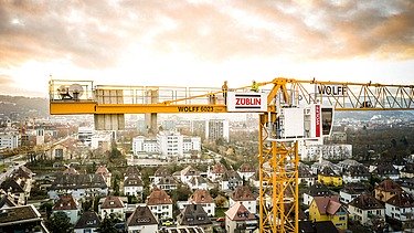 Gelber Kran mit Logos von Züblin und Wolff vor einem Stadtpanorama