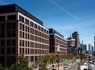 To kontorblokke med murstenslignende klinkefacader på en gade med træer