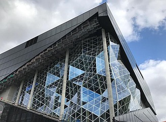 Blick aus der Froschperspektive auf eine Wabenartig strukturierte Glasfassade mit mehreren Säulen, die das Dach tragen