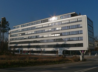 Plain white office building with 6 floors and recessed top floor, bare trees in the background