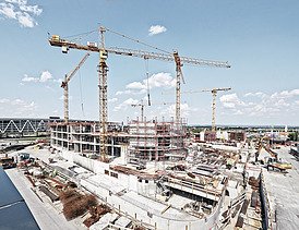 Cranes and skyscrapers under construction from a frog's-eye view against a blue sky