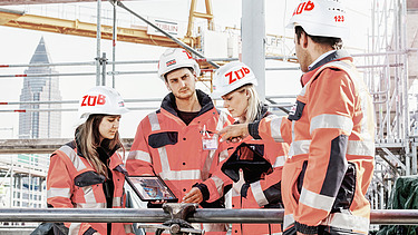 A group of people wearing helmets look at a tablet together