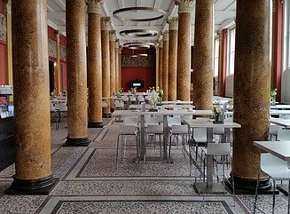 Hall with brown stone columns, terrazzo floor, white chairs and tables, window on the right side