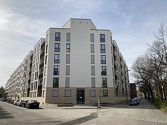 Das Bild zeigt eine Eckaufnahme eines Neubaus einer Wohnanlage mit beiger Fassade.