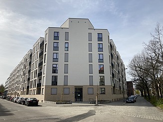Billedet viser et hjørnebillede af et nyt boligkompleks med en beige facade.