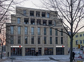 Commercial building with stepped façade, stores below, above two storeys with tall narrow windows, above two storeys with rectangular windows, white and red lettering