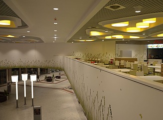 Hallway in a shopping center, stores to the right and left, benches and planters in the middle, a rotunda in the foreground