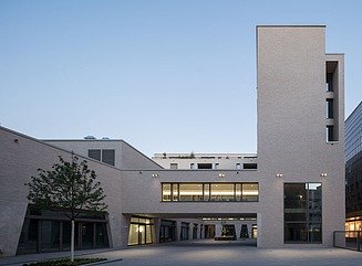 Sandsteinfassade mit groer Fensterfront, in der sich die Fassade einer neogotischen Kirche spiegelt, Fußgängerbrücke mit Fenstern, im Innenhof Arkaden