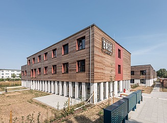 Several residential buildings with wooden cladding and brick-red accents on the two storeys above the first floor.