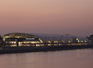 Two round buildings with illuminated windows, connected by a curved roof over both parts of the building
