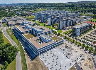 University campus from above with three flat blocks and parking lot in the foreground and 5 block-shaped buildings behind them
