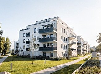 Staggered white apartment buildings with large balconies with black railings, lawns between the houses
