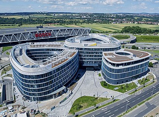 Three six-storey curved façades with windows, a green space in front and passers-by