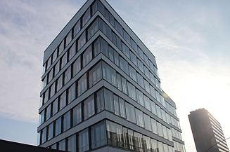 Hvid bygning med butiksvinduer i stueetagen, ADAC-bogstaver på den hvide overflade, 5 etager over, gult ADAC-logo på bygningen