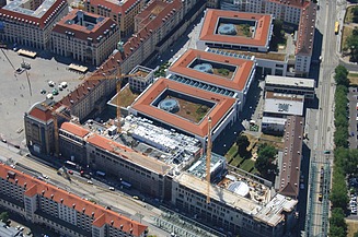 Fireetagers hjørnebygning i wilhelminsk stil med arkade på en stor plads med biler og fodgængere i forgrunden