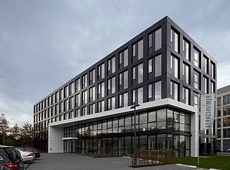 Hjørnebygning med sort facade, høje smalle vinduer og skråtstillet hvid baldakin over indgangen