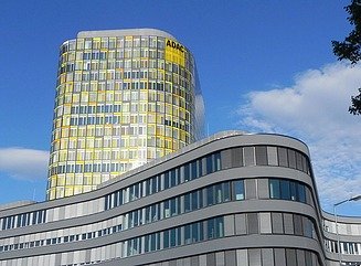 Curved façade five-storey façade with windows, behind it a tower with rounded corners and yellow color reflections, above the ADAC logo, Saturn lettering above the entrance