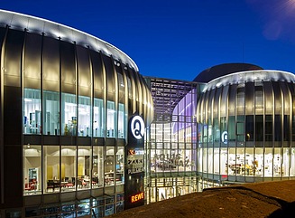 Zwei runde Glasgebäude, verbunden durch eine Passage, über dem Eingang der Schriftzug Aquis Plaza in rot