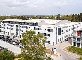 Hvid bygning, parkeringsplads og træer i forgrunden