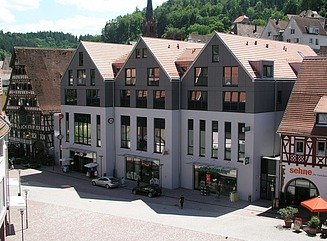 Gågade med tre let forskudte hvide beboelseshuse med sorte gavle, røde tage og mange vinduer, butikker med udstillingsvinduer nedenunder