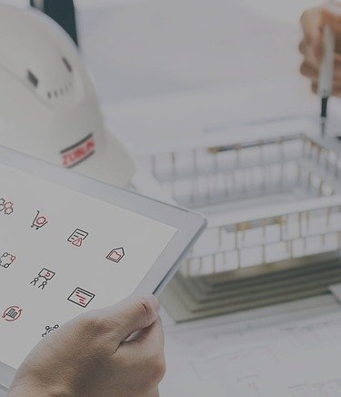 OpenTools Header Nahaufnahme eines Schreibtischs mit Züblin Helm, zwei Hände halten ein Pad mit den Icons für OpenTools, die Hände einer weiteren Person mit Stift