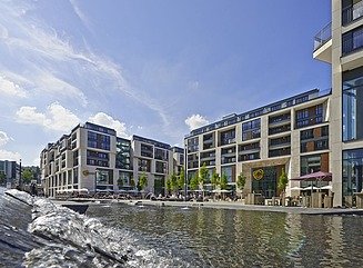 Vand i forgrunden, bagved et lyst shoppingcenter i tre etager med store vinduesfacader