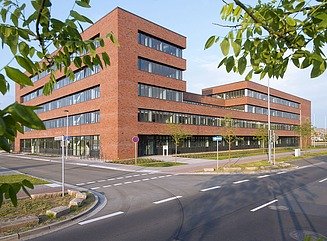 Stark perspektivisch dargestellte Backsteinfassade mit dunkler Fensterfront ,am Ende ein nahezu quadaratischer Aufbau mit zwei Stockwerken und nd durchgehenden Fensterfronten
