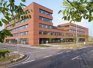 Brick façade with a dark window front shown in strong perspective, at the end an almost square structure with two storeys and continuous window fronts