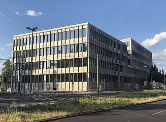 Bürogebäude mit strukturierter Fassade, hohen schmalen Fenstern und Eingangsbereich mit Säulen