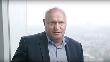 Jens Quade vor einem Fenster mit Stadtpanorama im Hintergrund