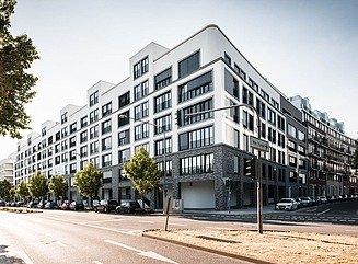 Lyst boligbyggeri i flere etager med tilbagetrukket øverste etage, tre træer foran