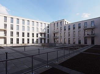 Indre gårdsplads med rækværk i forgrunden, omgivet af to fløje af en hvid bygning med smalle, høje vinduer