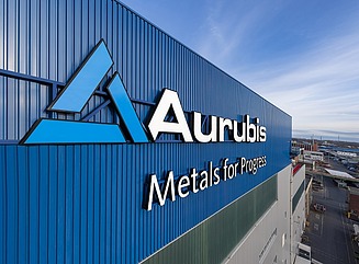 Rasen mit Bäumen und Sträuchern im Vordergund, dahinter ein fünfgeschossiger weißer Bürobaukomplex mit großen Fenstern