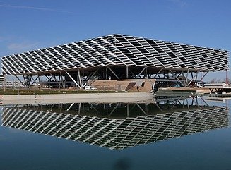 Gebäude auf Stelzen und mit strukturierter Fassade spiegelt sich im Wasser
