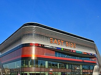 Rounded façade of a shopping center with the lettering East Side, high window fronts on the first floor and red elements above
