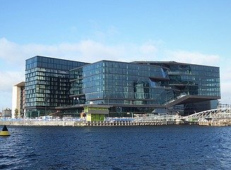 Block of three buildings with glass facades on the waterfront, with three boats on top