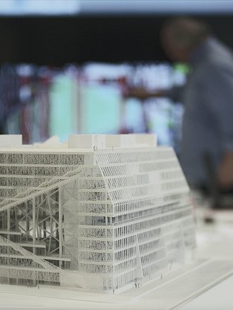 Modell eines Gebäudes im Vordergrund mit Menschen und Leinwand im Hintergrund