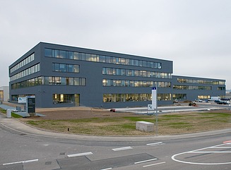 Trin til en glaseret portal, baldakinen har indbyggede lys, en mørk væg til højre, vinduer til venstre