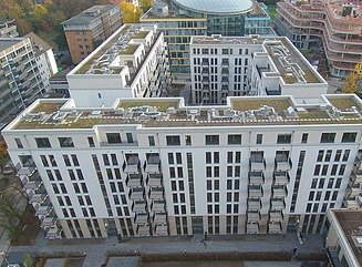 Mehrere Riegel mit Mehrfamilienhäusern, weiße Fassaden und Balkone um einen Innenhof mit Grünflächen