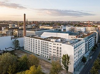 Siebengeschossiger Wohnbau, im Vordergrund Bäume, im Hintergrund Blick über die Stadt