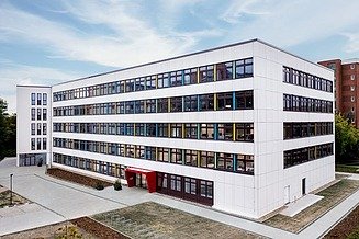 Das Bild zeigt ein weißes Bürogebäude mit rotem Eingangsbereich