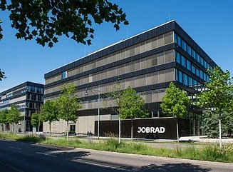 Eckgebäude mit horizontaler Gestaltung der Fenster, schwarze Verkleidung, vor dem Gebäude Bauzaun mit Aufschrift Milestone